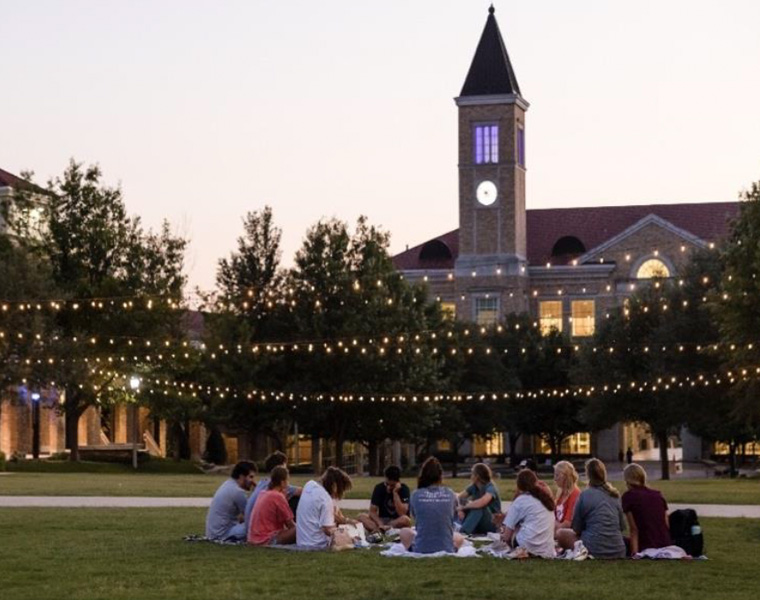 Students gathering on lawn in Campus Commons at dusk
